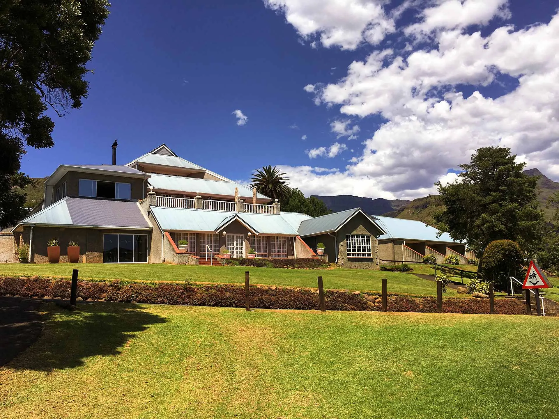 The white hotel buildings on their lawn beneath the Drakensberg