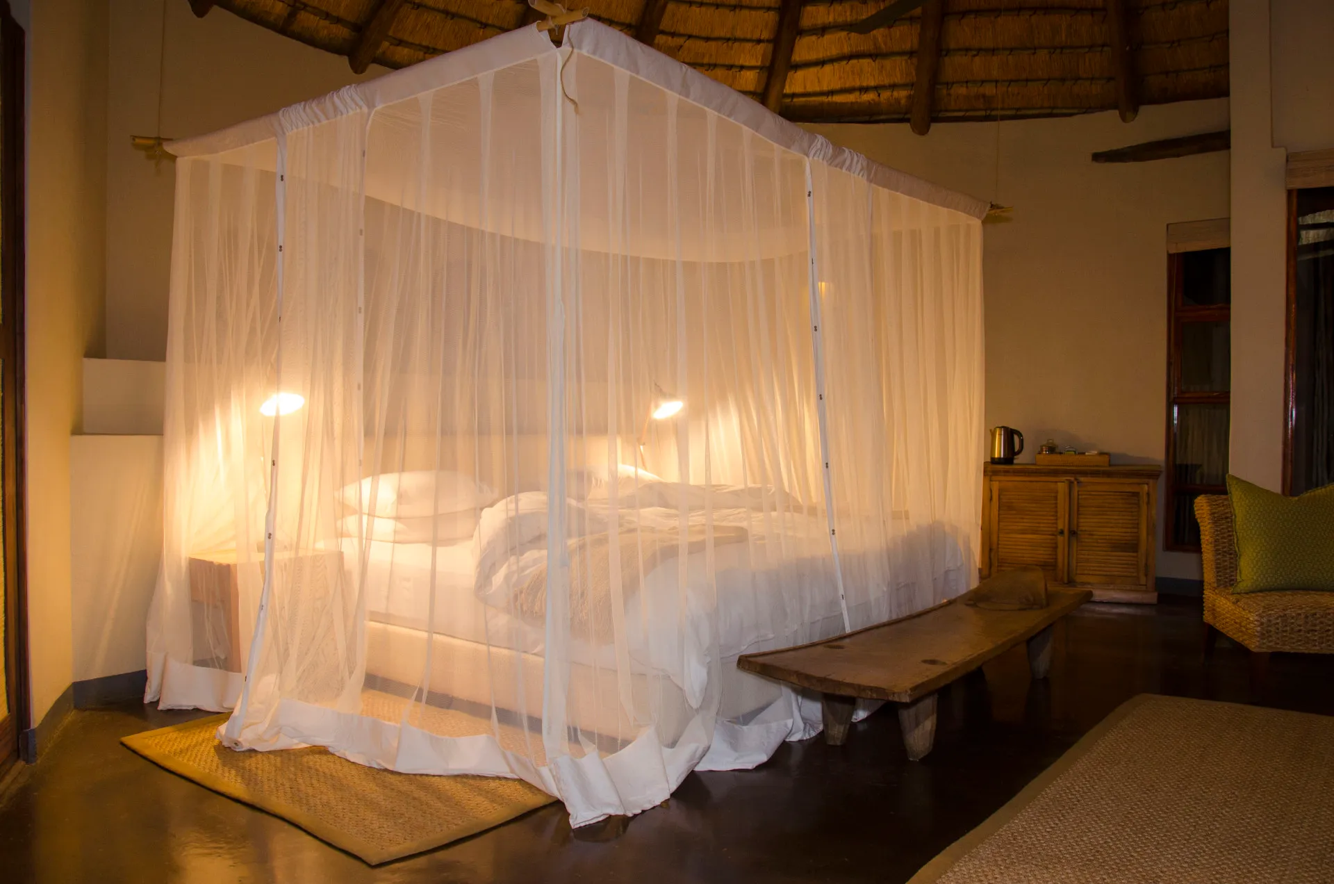 A four-poster bed under a mosquito net beneath a thatched roof