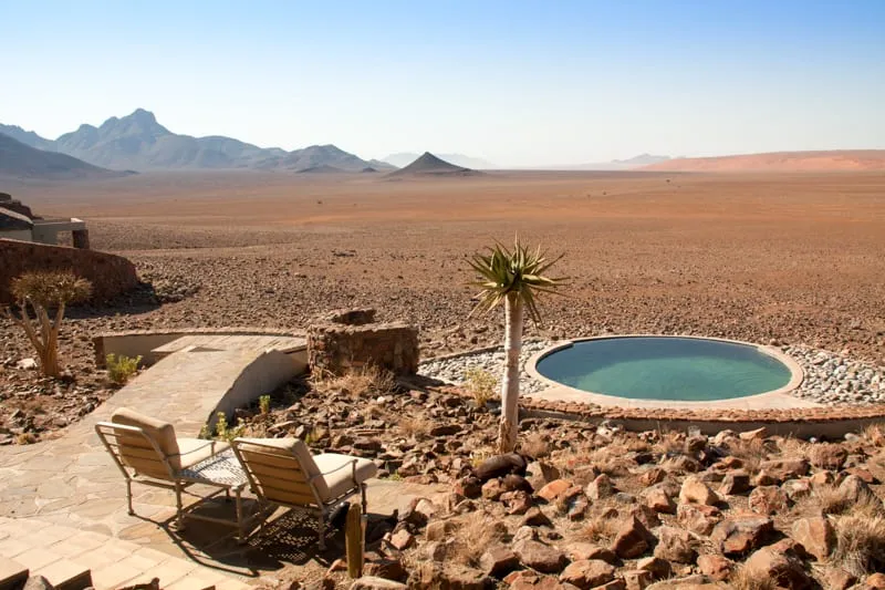 Loungers beside a plunge pool cut into the rock, looking out over the Namib plain