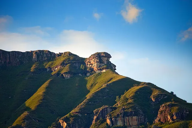 A high rock buttress catching the light above green slopes